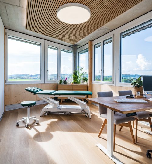 Behandlungszimmer sehr hell mit viel holz und grüne Behandlungsliege